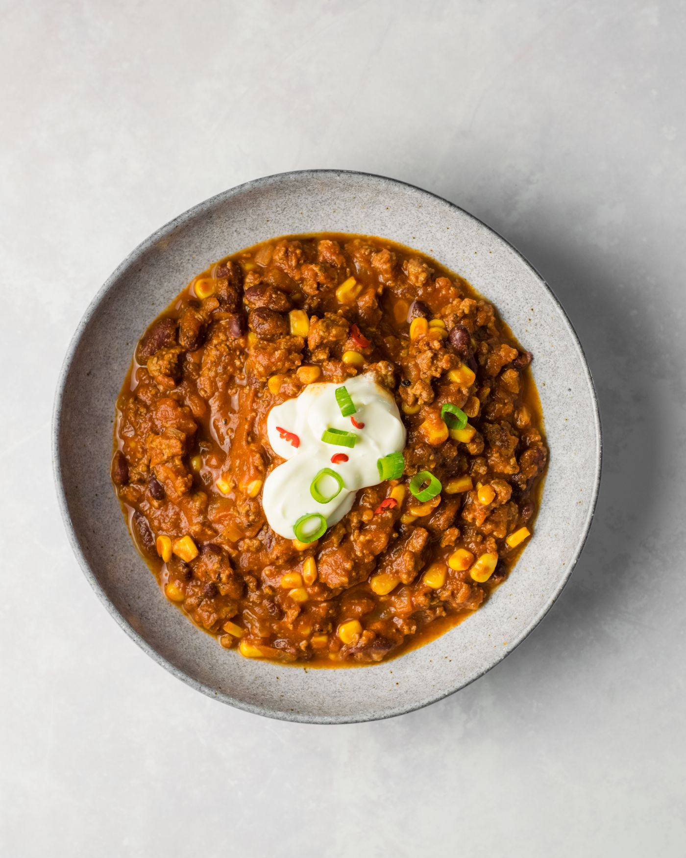 Beef, bean and corn chili. ground meat crumbles; kidney beans; yellow corn; red-brown tomato base; sour cream; scallion rings.